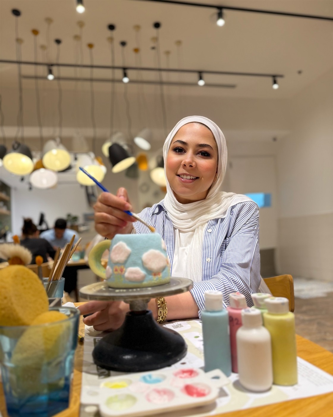 Merit smiling while painting a colorful teapot at an art café